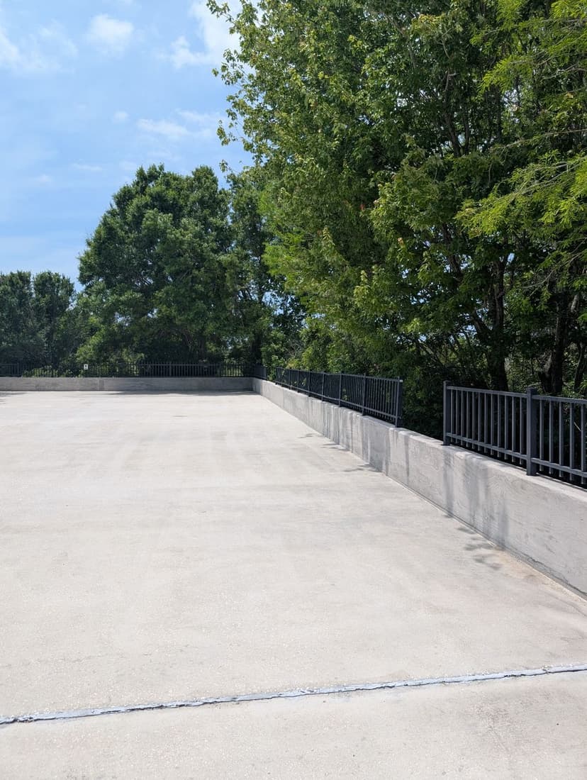 Empty parking lot with a clear sky and surrounding trees providing shade.
