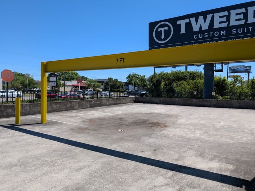 Yellow height clearance bar marked 7FT in empty parking lot near Tweed Custom Suits.
