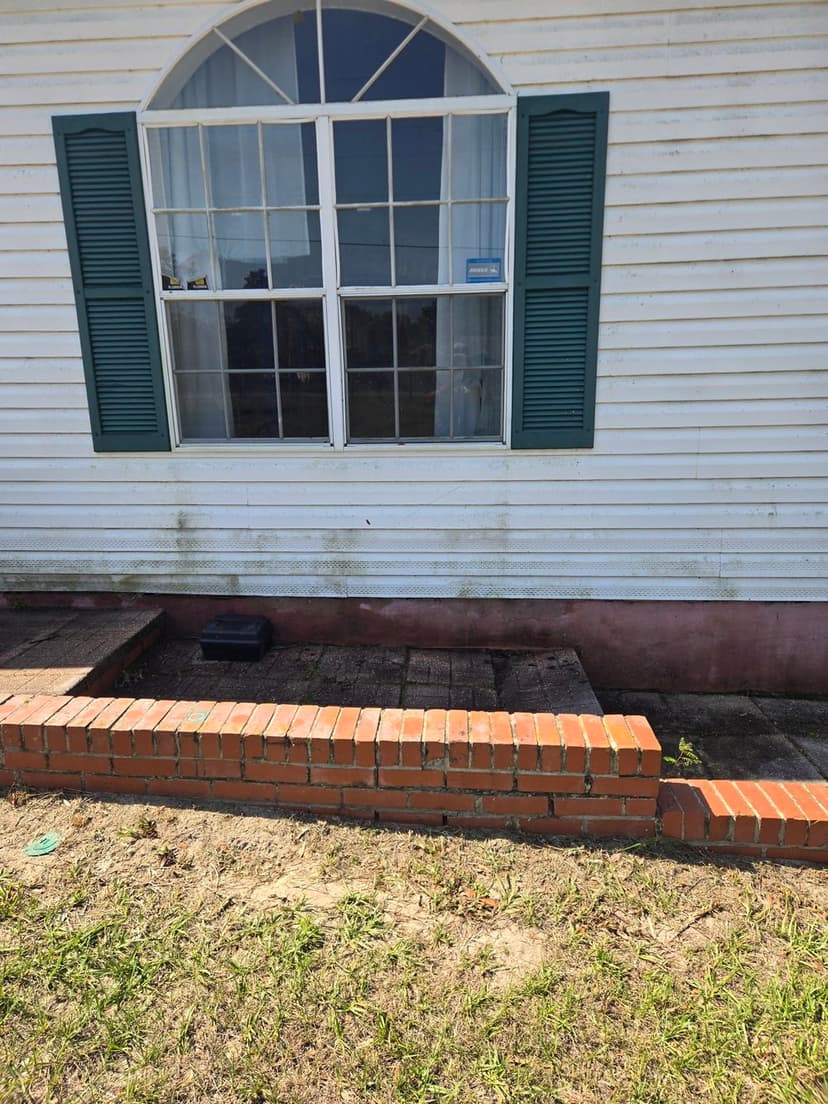 Exterior view of a house with a window, green shutters, and a brick foundation.